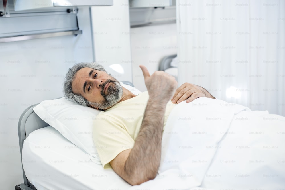 Porträt eines pensionierten älteren Mannes, der während des Coronavirus-Covid-19-Ausbruchs langsam atmet. Alter kranker Mann liegt im Krankenhausbett und wird wegen tödlicher Infektion behandelt