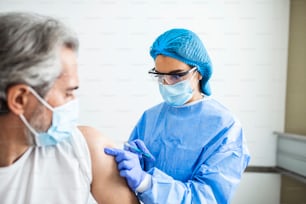 注射器を持ち、医療用マスクで患者に注射する前に綿を使用する医師をクローズアップします。Covid-19またはコロナウイルスワクチン