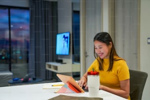 Bella donna asiatica che utilizza la tavoletta digitale con internet per il lavoro di piccole imprese in appartamento di notte. Digitazione freelance femminile sulla tastiera del tablet per lavoro online o shopping a casa.