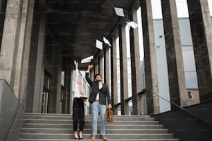Hombre y mujer árabes alegres con ropa formal vomitando algunos documentos mientras están parados en las escaleras al aire libre. Concepto de proyecto común y cooperación exitosa.