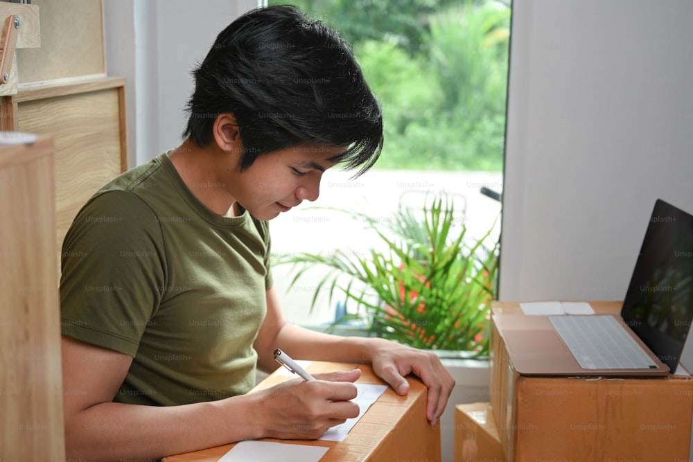 Jeune entrepreneur en démarrage écrivant l’adresse sur une boîte en carton pour la livraison au client.