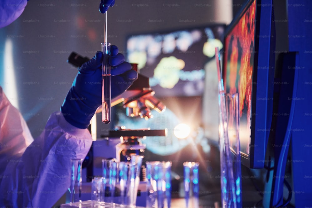 Scientist in white protective uniform works with coronavirus and blood tubes in laboratory.