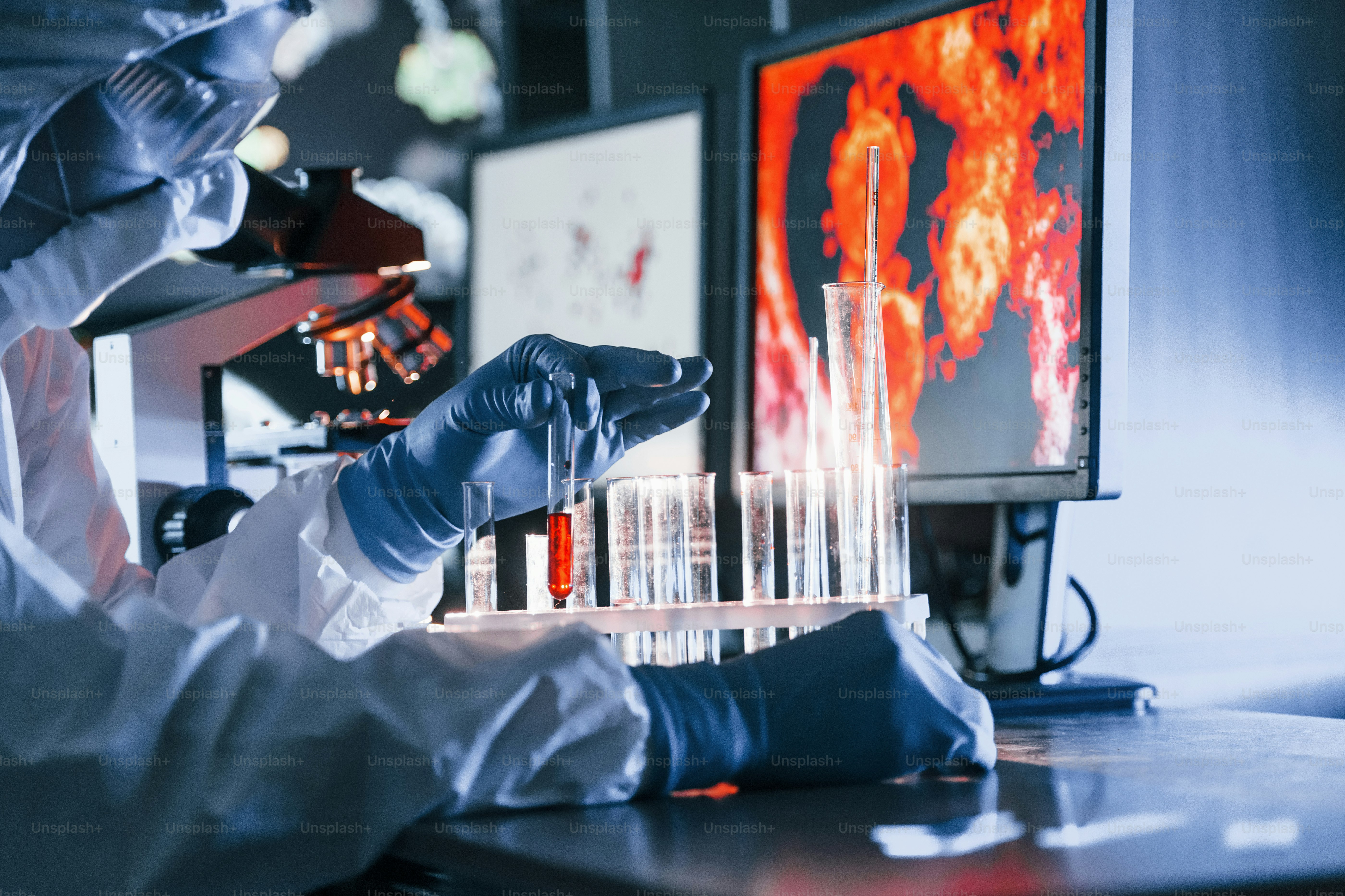 Un scientifique en uniforme de protection blanc travaille avec le coronavirus et des tubes sanguins en laboratoire.