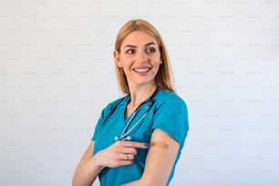 Portrait of a female doctor smiling after getting a vaccine. Medical worker showing her arm with bandage after receiving vaccination.