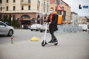 Coursier joyeux portant un sac à dos isotherme lors de la livraison de nourriture en scooter