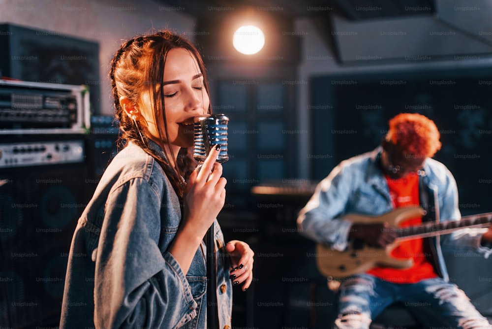 Guy plays guitar, girl sings. African american man with white girl rehearsing in the studio together.