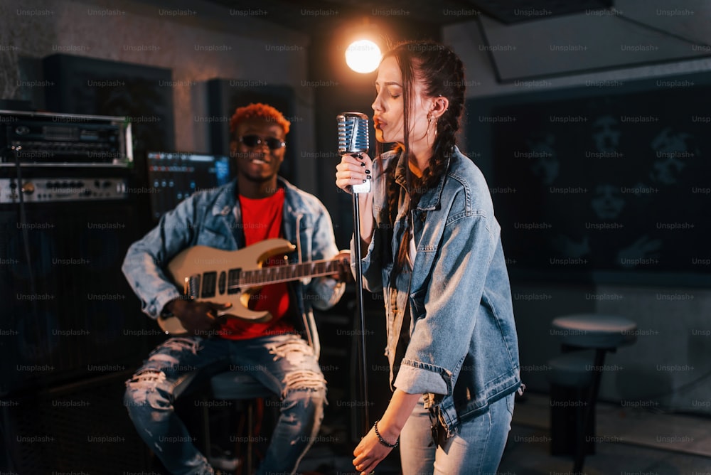 남자는 기타를 연주하고 여자는 노래합니다. 백인 소녀와 함께 스튜디오에서 리허설을 하는 아프리카계 미국인 남자.