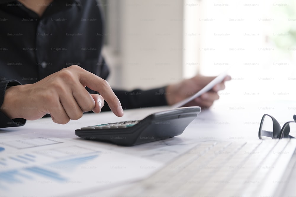 Concept de comptabilité d’entreprise, homme d’affaires utilisant une calculatrice avec un ordinateur portable, un budget et un papier de prêt au bureau.
