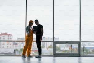 Female worker or engineer in yellow uniform and hard hat standing indoors with man.