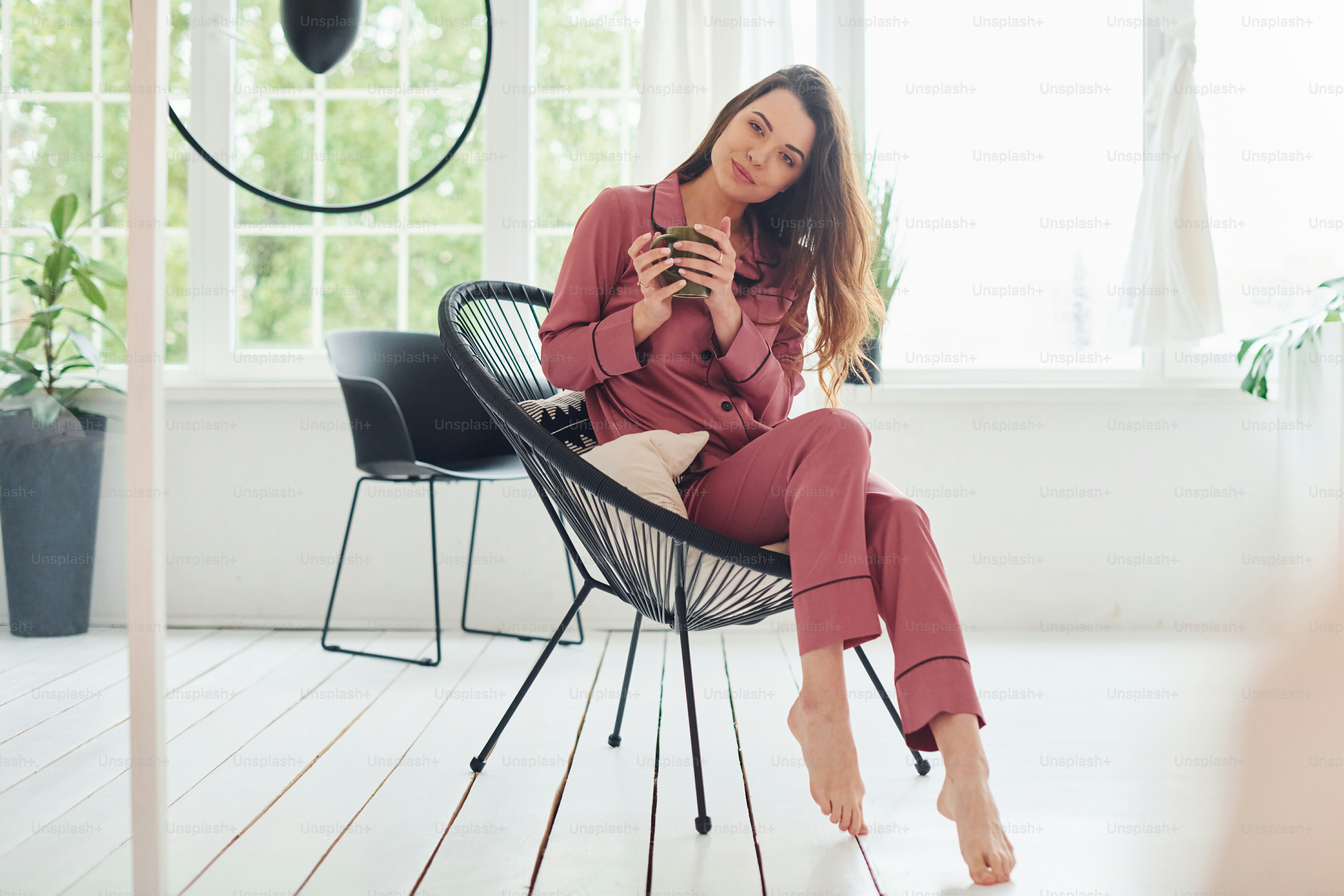 Cheerful young woman in pajamas sitting on the chair indoors at daytime.