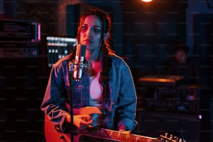 Jeune et belle interprète féminine avec guitare chantant et répétant dans un studio d’enregistrement.