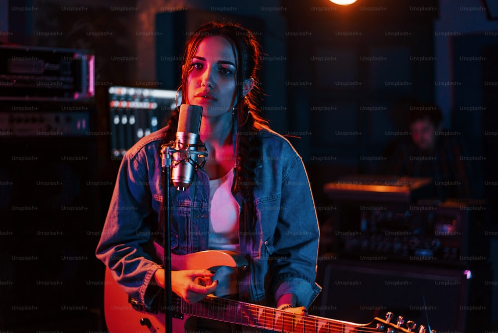 Young beautiful female performer with guitar singing and rehearsing in a recording studio.