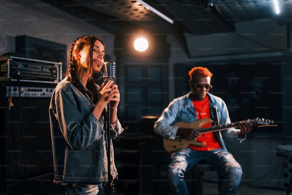 男はギターを弾き、女の子は歌う。白人の女の子と一緒にスタジオでリハーサルをしているアフリカ系アメリカ人の男性。