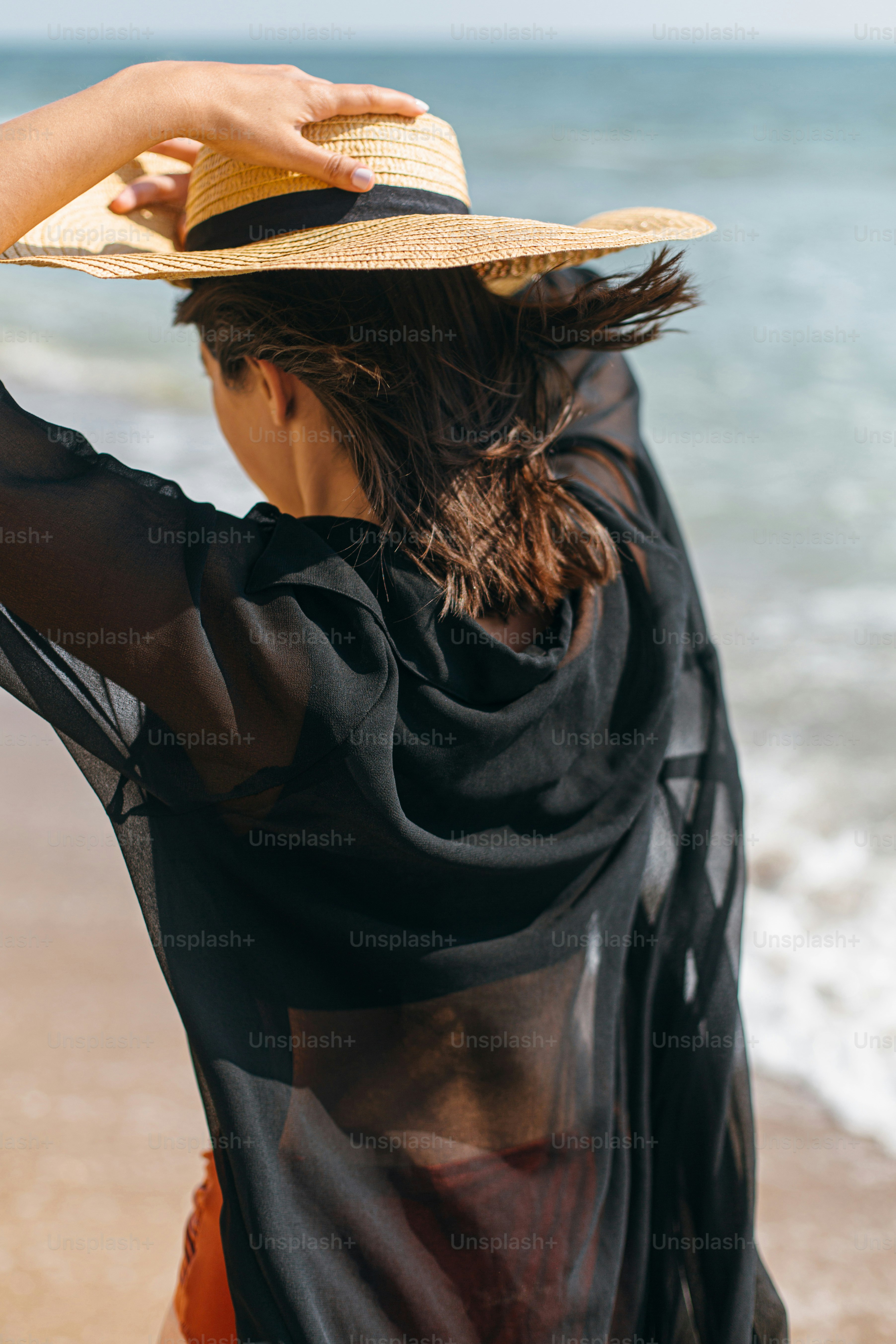Hermosa mujer elegante con sombrero que camina en la playa ventosa en las olas del mar. Veraneo. Ajuste sexy mujer joven en camisa ligera y sombrero de paja relajándose en una isla tropical