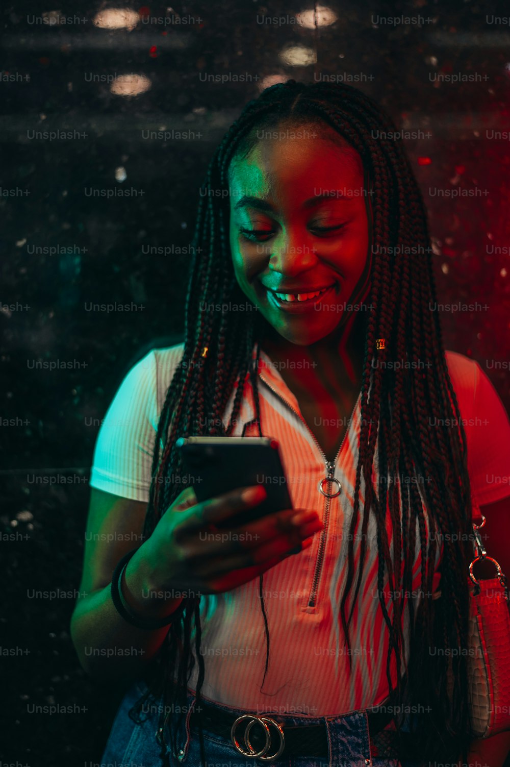 Young cheerful african american woman using smartphone while in the subway metro station and being illuminated by the green and red light in the night