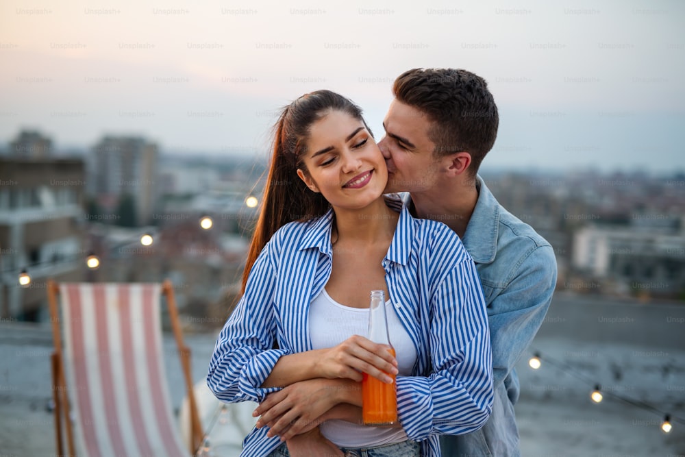 Jeune couple heureux amoureux s’amusant lors d’une fête sur le toit au coucher du soleil.