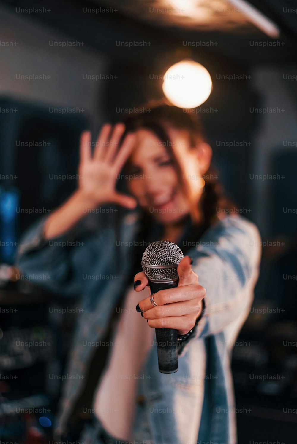 Close up view of microphone. Young beautiful female performer rehearsing in a recording studio.