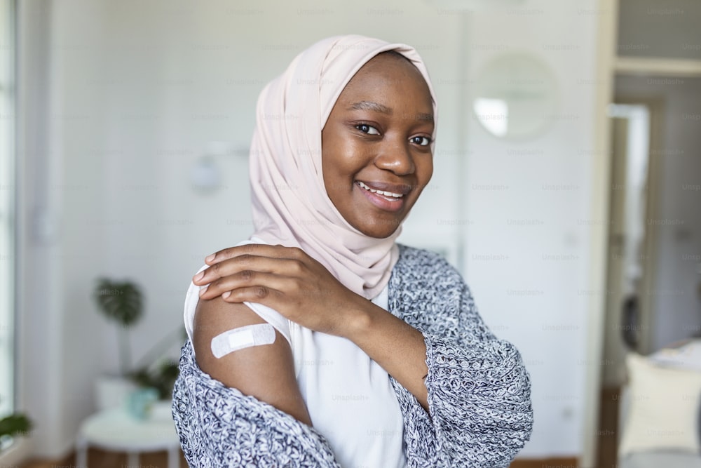 Vendaje adhesivo en el brazo después de la inyección de vacuna o medicamento,VENDAS ADHESIVAS YESO - Equipo médico,Venda adhesiva de enfoque suave en un braquio femenino musulmán africano después de la vacunación covid-19