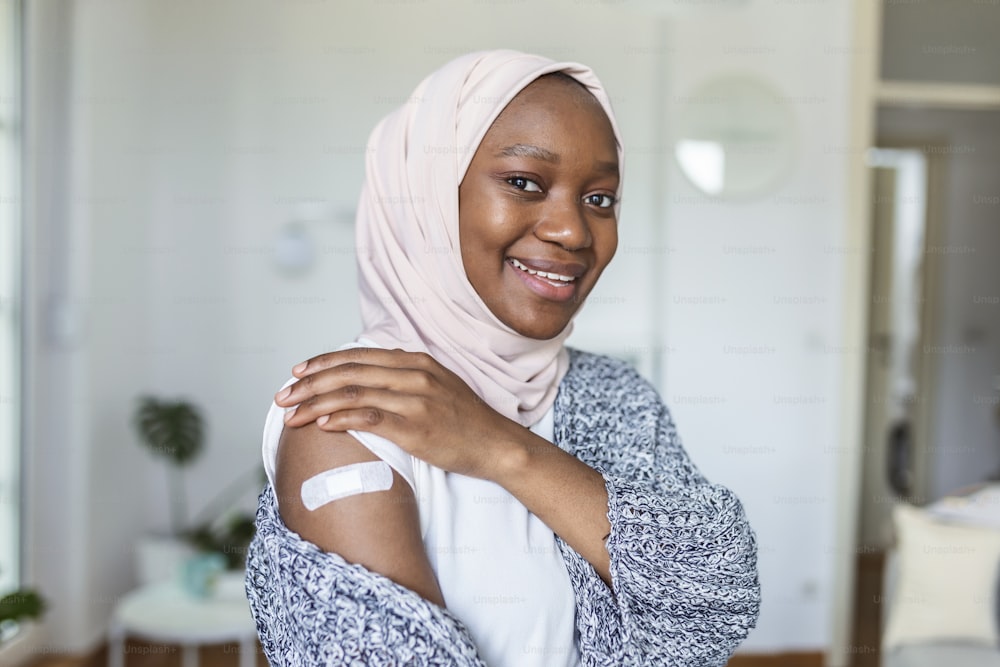 Klebeverband am Arm nach Injektion Impfstoff oder Medizin,KLEBEBANDAGEN PFLASTER - Medizinische Geräte,Weichzeichner Klebeverband an einem muslimischen afrikanischen weiblichen Brachium nach Covid-19-Impfung