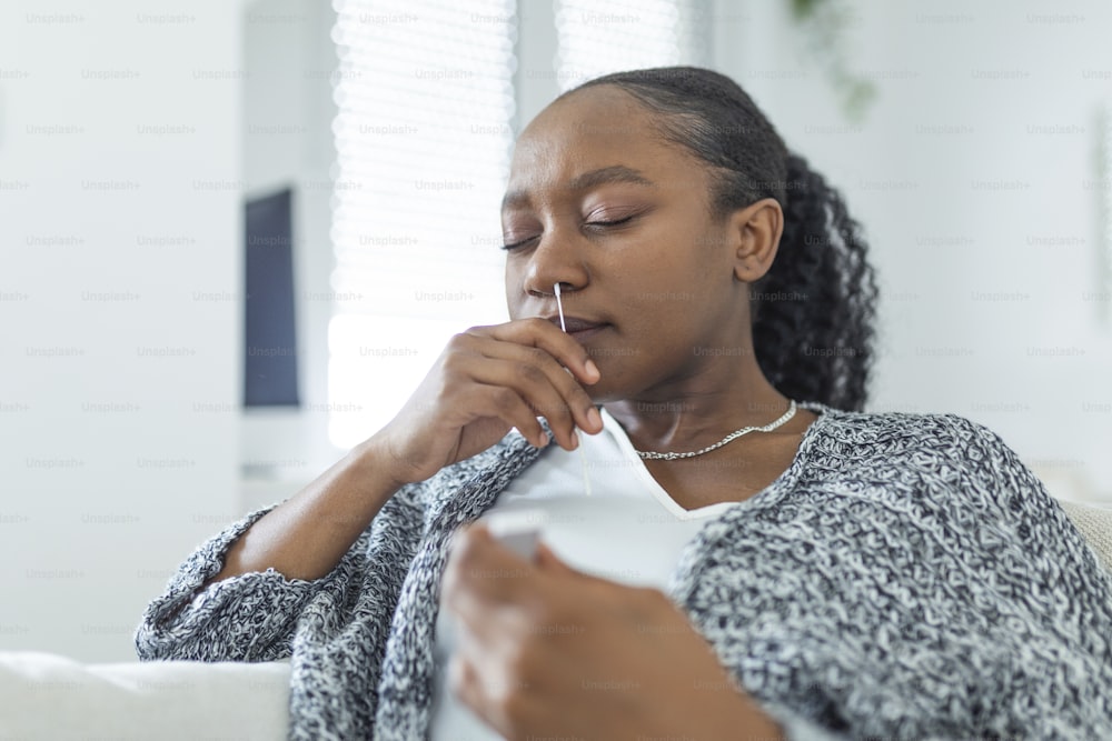 自宅でコロナウイルスPCR検査をしながら綿棒を使用するアフリカ系アメリカ人の女性。コロナウイルス迅速診断検査を使用している女性。COVID-19のために鼻腔ぬぐい液を使用している自宅で若い女性。
