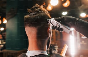 Close up view of young bearded man that sitting and getting haircut in barber shop.