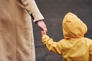 Kid in yellow waterproof cloak holding mother's hand and have a walk outdoors.