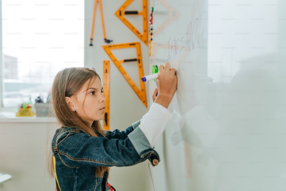 現代の学校の教室で黒板にフェルトチップで書く小学生。新学期のコンセプト。セレクティブフォーカス。