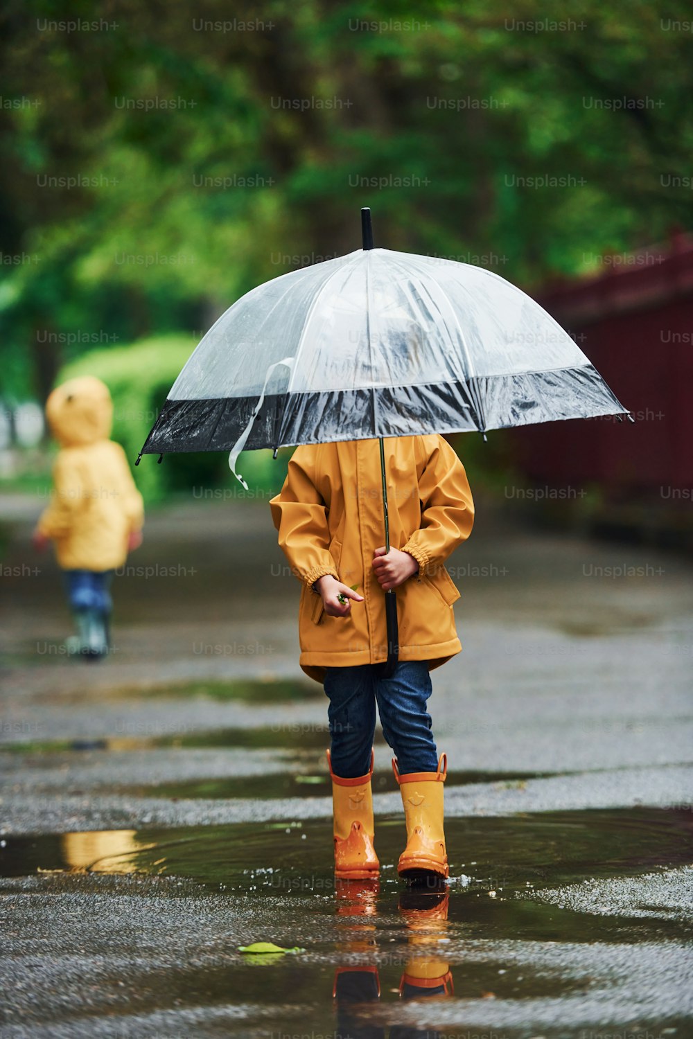 Two kids with umbrella in yellow waterproof cloaks and boots playing outdoors after the rain together.