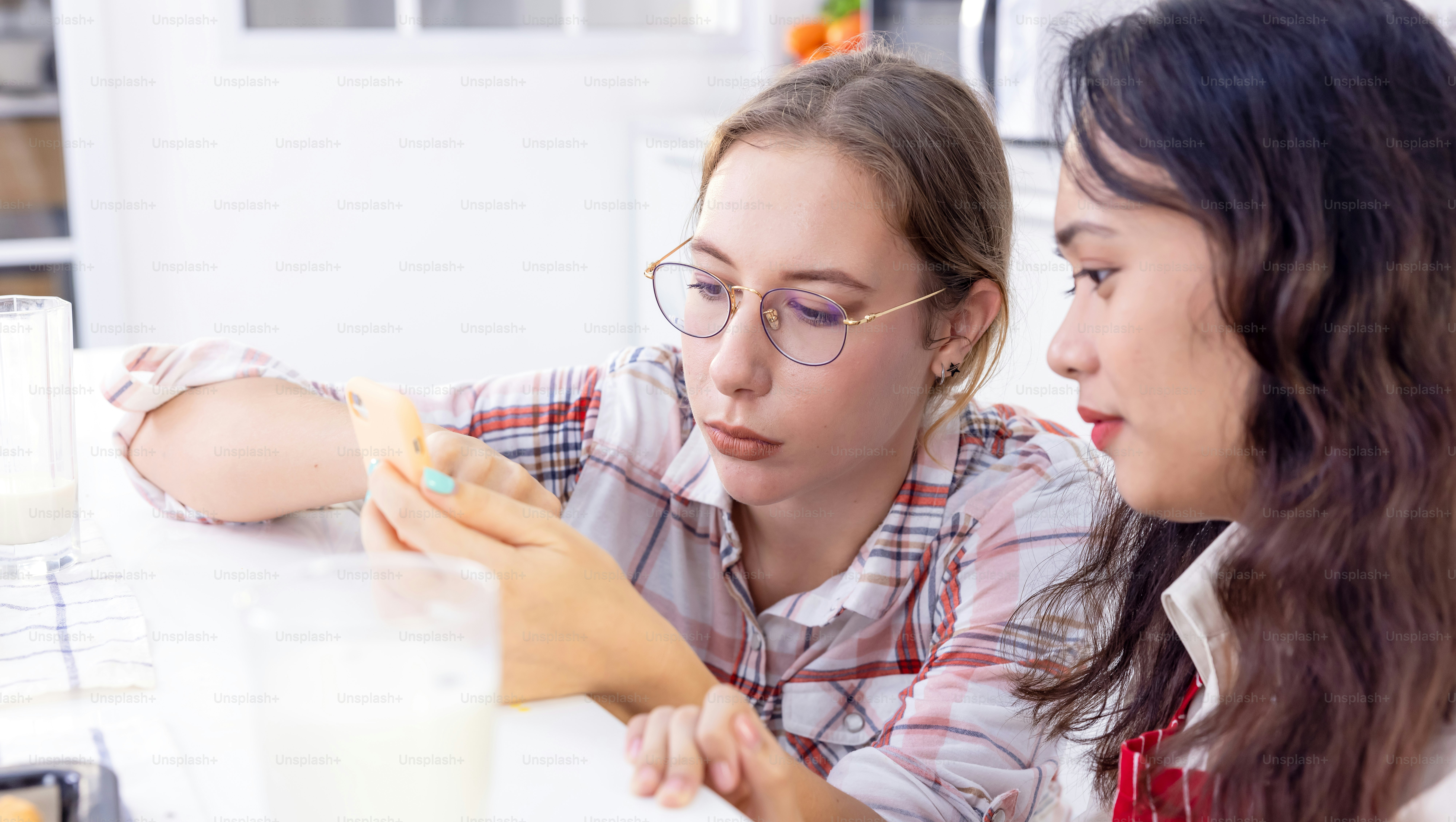 Two friends in kitchen, Woman at breakfast table Looking at Partner Messaging On Social Media