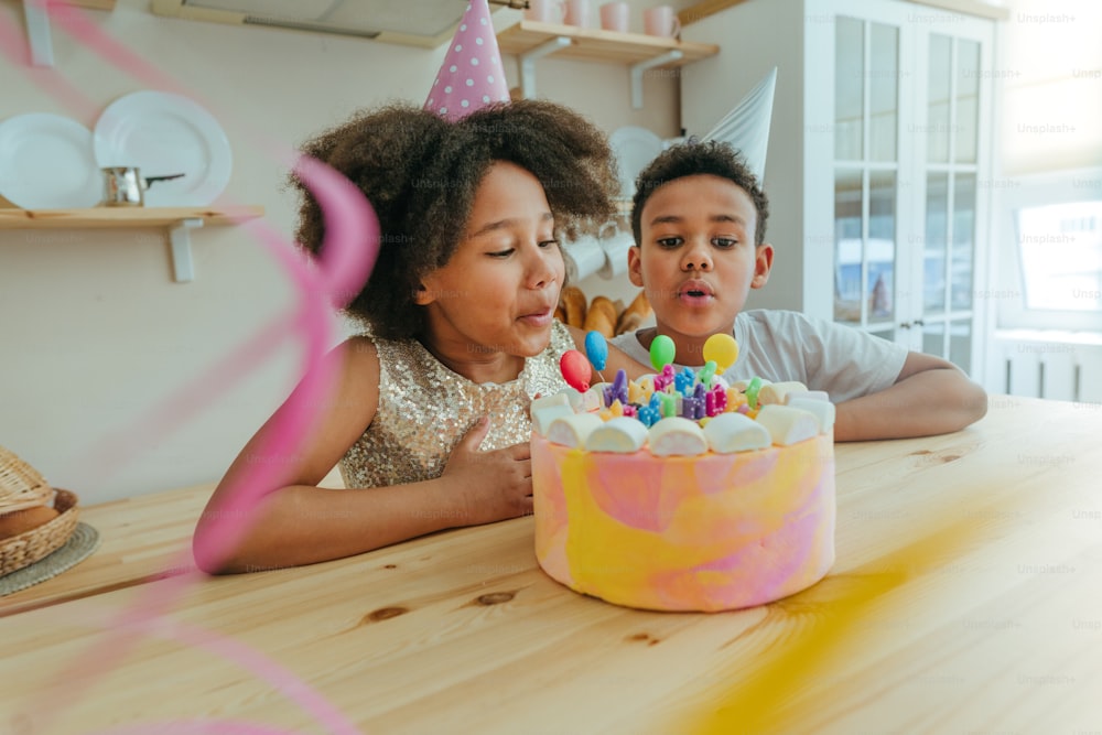 Chica feliz mirando el pastel de cumpleaños con velas divirtiéndose durante la fiesta de cumpleaños en la cocina. Enfoque selectivo en el rostro de la niña.