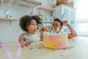 キッチンでの誕生日パーティー中に楽しい時間を過ごしているキャンドル付きのバースデーケーキを見ている幸せな女の子。女の子の顔に選択的に焦点を合わせます。