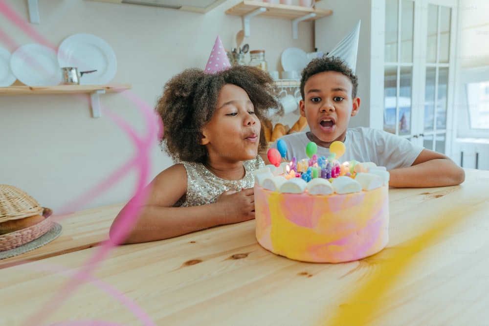 Happy girl looking at the birthday cake with candles having fun time during birthday party in the kitchen. Selective focus on the girl's face.