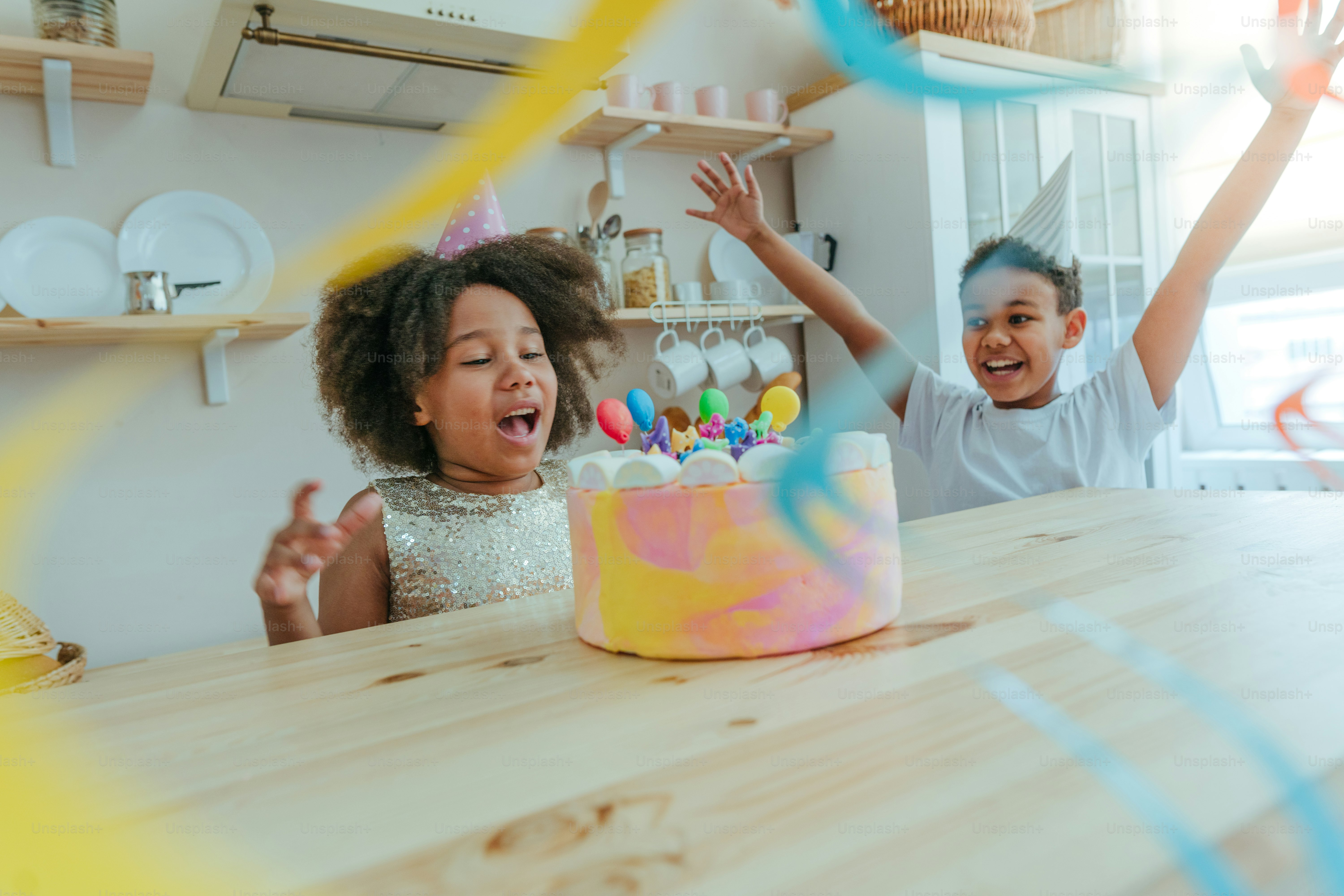 Happy girl looking at the birthday cake with candles having fun time during birthday party in the kitchen. Selective focus on the girl's face.