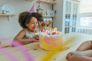 Glückliches Mädchen, das den Geburtstagskuchen mit Kerzen betrachtet und Spaß während der Geburtstagsfeier in der Küche hat. Selektiver Fokus auf das Gesicht des Mädchens.