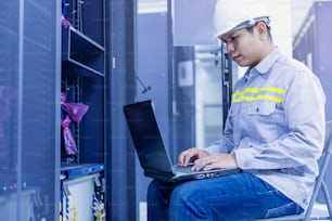 Network administrator holding laptop in hand working Configuration with core switch on rack cabinet in data center