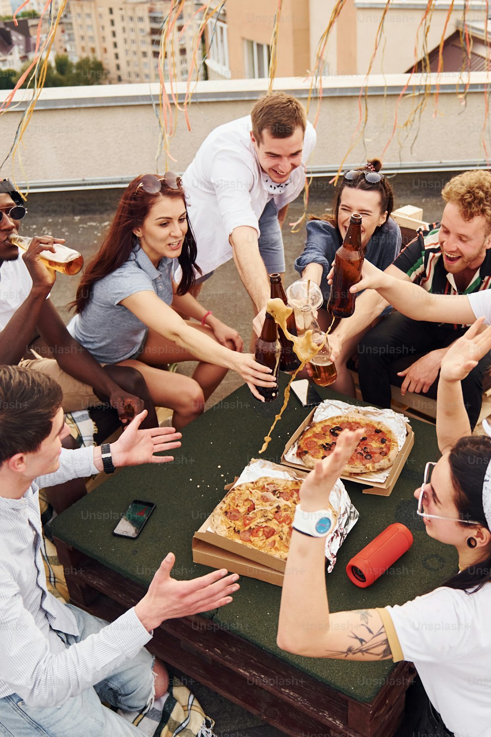 Fare applausi da bottiglie con birra. Un gruppo di giovani in abiti casual fa una festa insieme sul tetto durante il giorno.