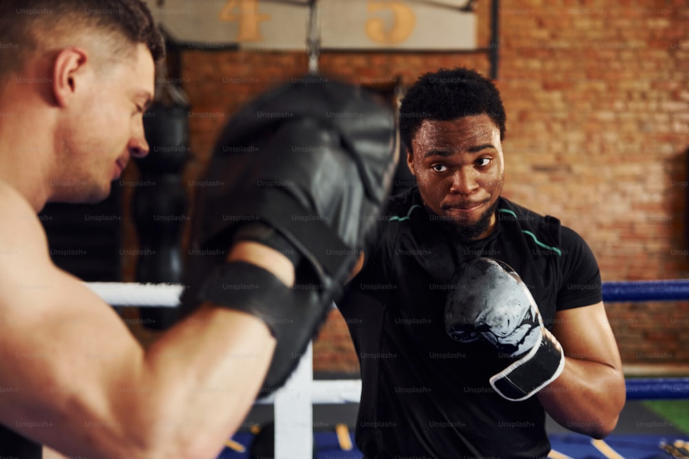ボクシングの練習をする。白人の男を持つアフリカ系アメリカ人の男性は、ジムでトレーニングの日を過ごしています。