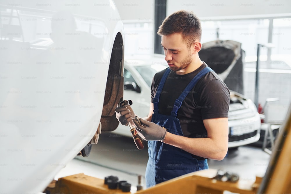 Un homme en uniforme de travail répare une voiture à l’intérieur. Conception d’un service automobile.