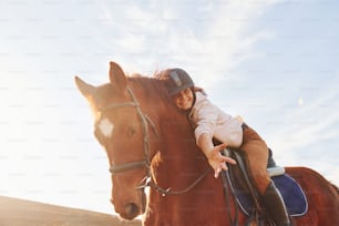 Junge Frau mit Schutzhut mit ihrem Pferd auf dem Acker am sonnigen Tag.