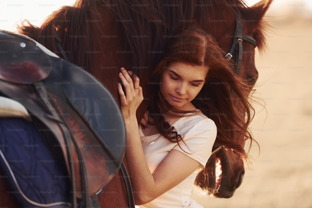 Young woman embracing her horse in agriculture field at sunny daytime.