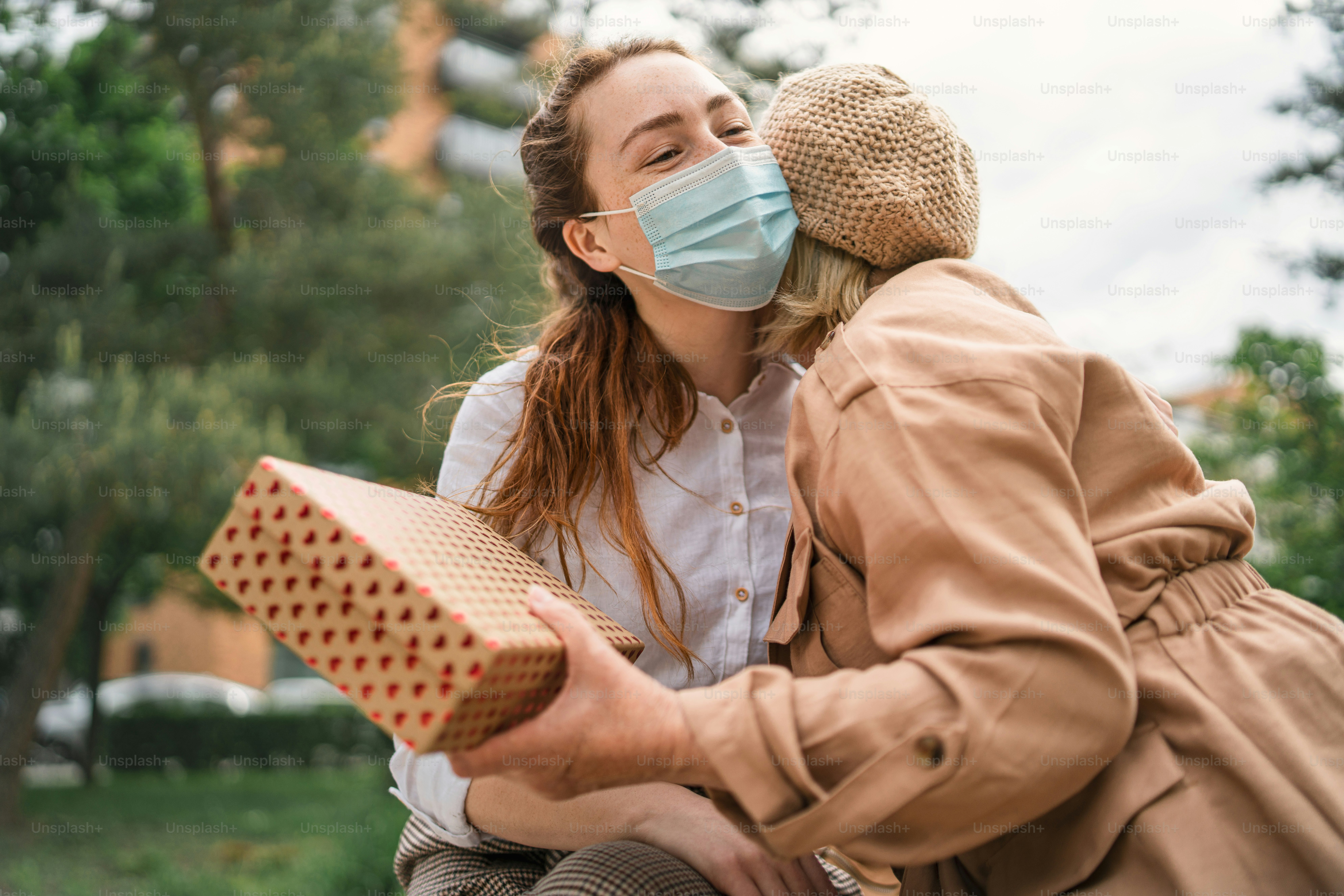 A young woman giving present and hugging grandmother outdoors in city, life after covid-19 vaccination.