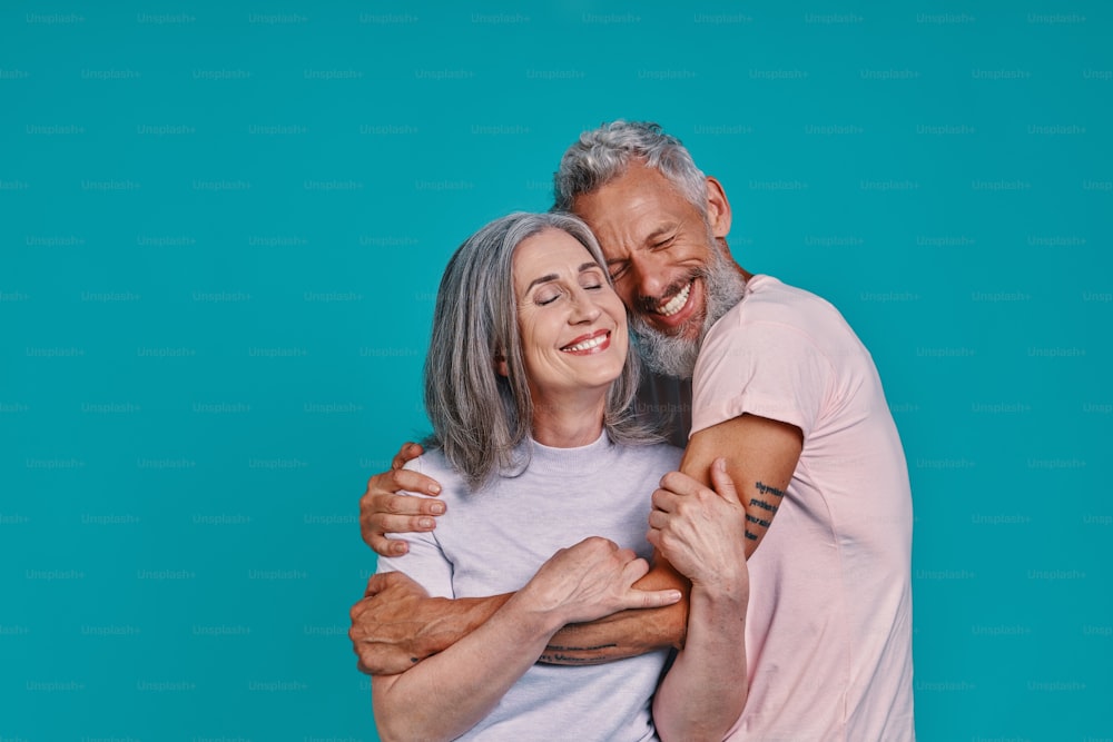 Loving senior couple bonding and smiling while standing together against blue background
