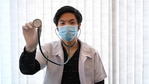 Doctor in protective mask holding stethoscope while standing in hospital.