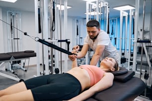 Young woman on massage bed with expander simulator. Physical therapist treats injury to shoulder and arm in physiotherapy room. Masseur treats athlete female patient after sports injury