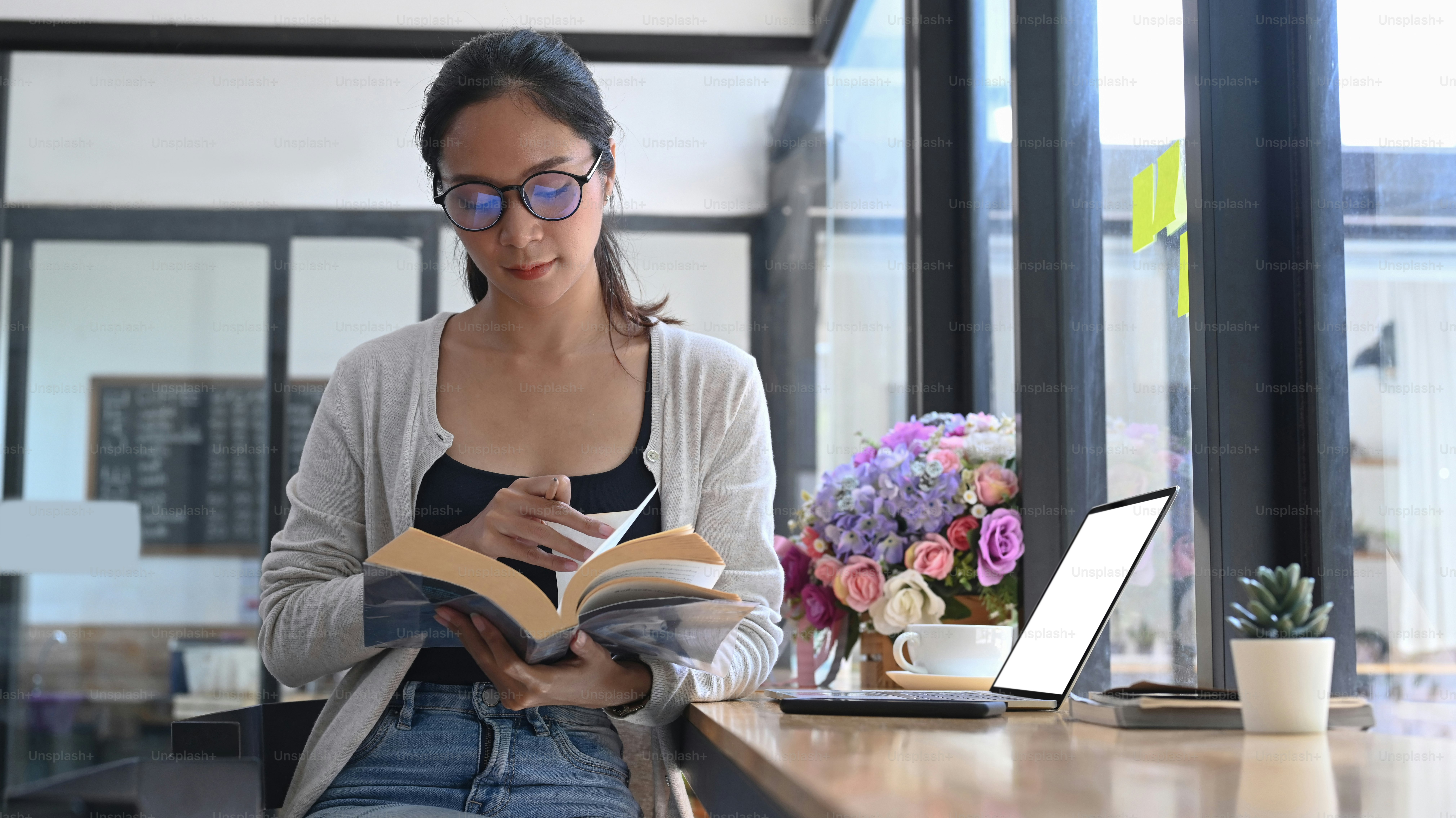 Casual young woman reading book in modern coffee shop.