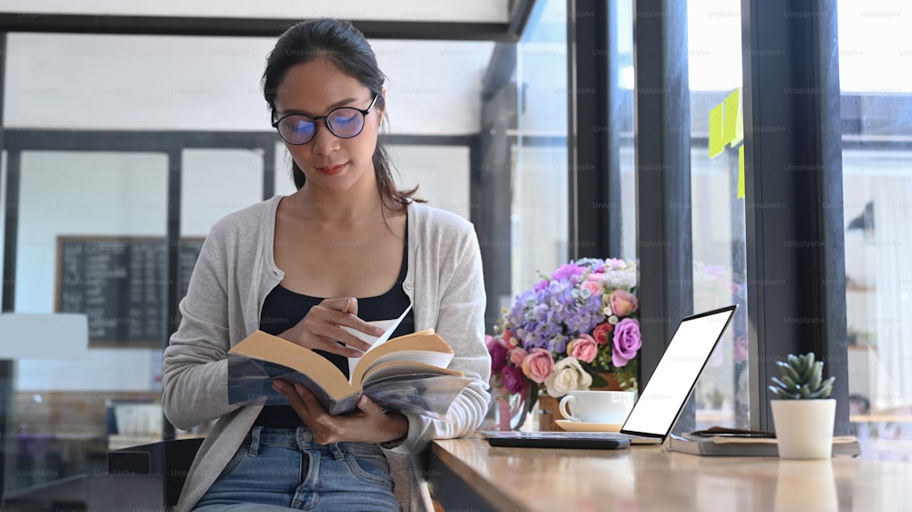 Casual young woman reading book in modern coffee shop.