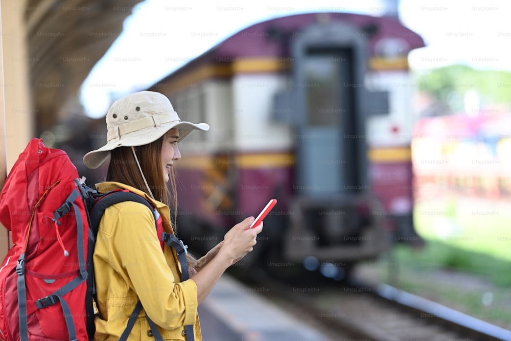 Young woman traveler with backpack using smart phone and standing in the railway.