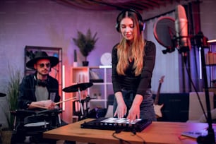 Caucasian man playing electronic drums while woman mixing sound on equalizer. Talented duo of musicians working on new song at professional music studio.