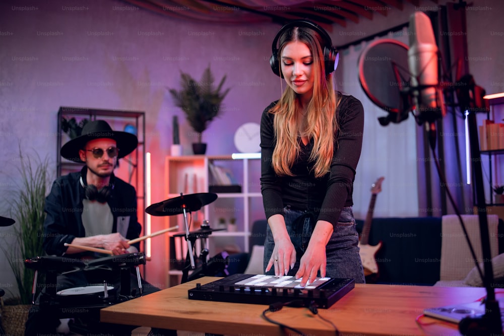 Uomo caucasico che suona la batteria elettronica mentre la donna mescola il suono sull'equalizzatore. Talentuoso duo di musicisti che lavorano su una nuova canzone in uno studio musicale professionale.