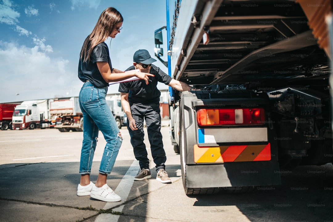Two professional truck drivers stand in front of the big truck. They talk and perform a technical inspection of the vehi